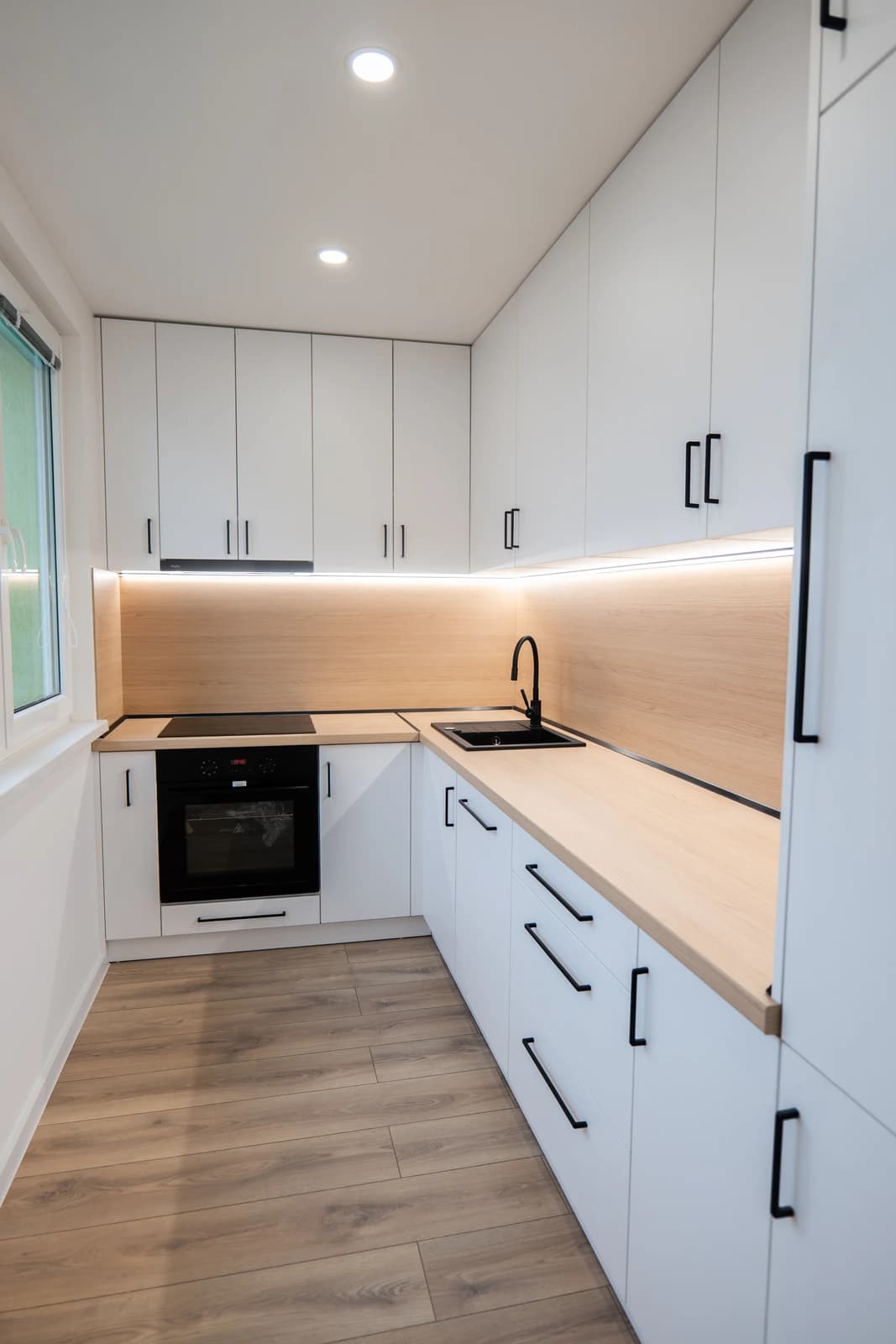 Štýlová tmavá kuchyňa s moderným osvetlením, zlatými akcentmi a elegantným jedálenským stolom.