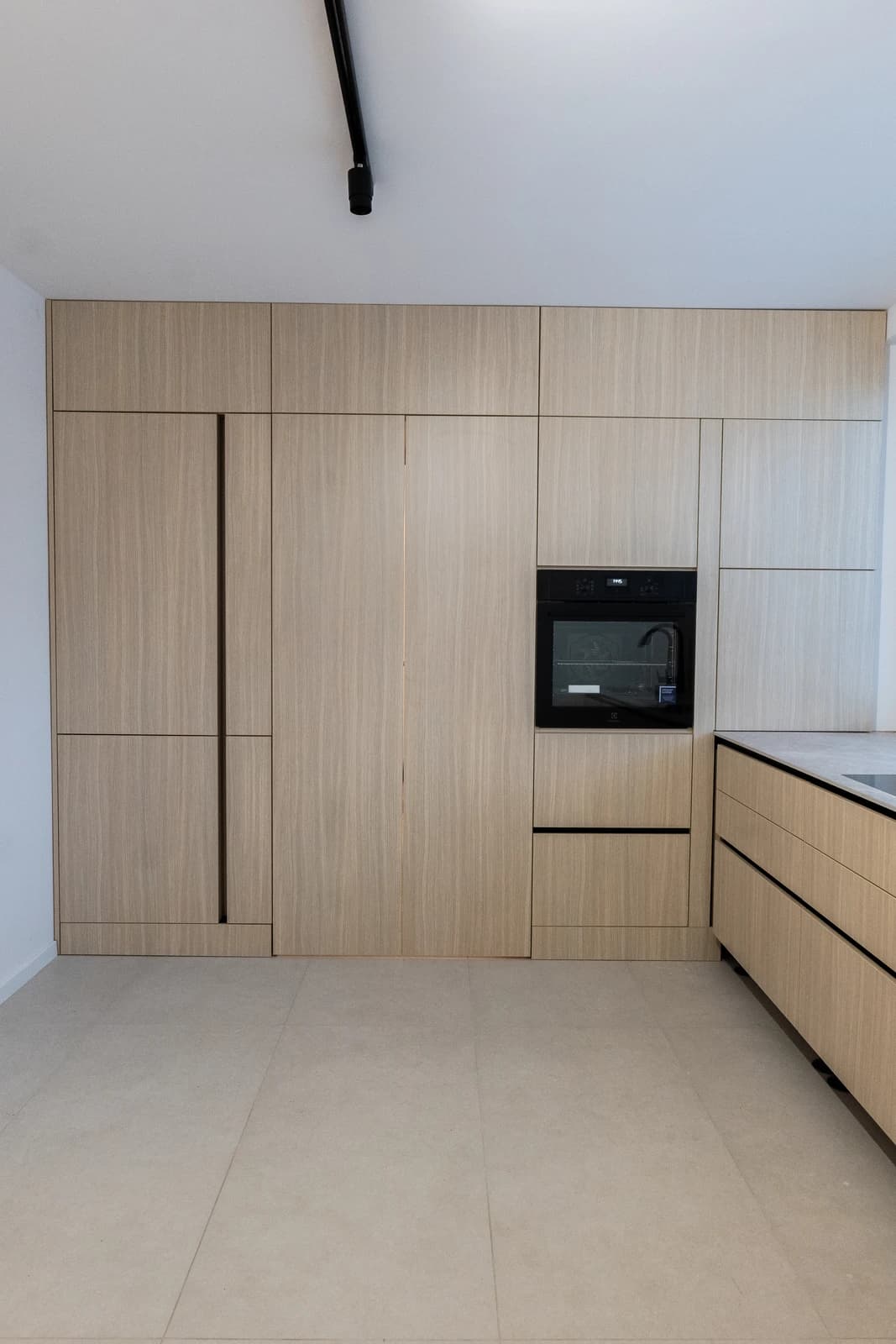 Štýlová tmavá kuchyňa s moderným osvetlením, zlatými akcentmi a elegantným jedálenským stolom.