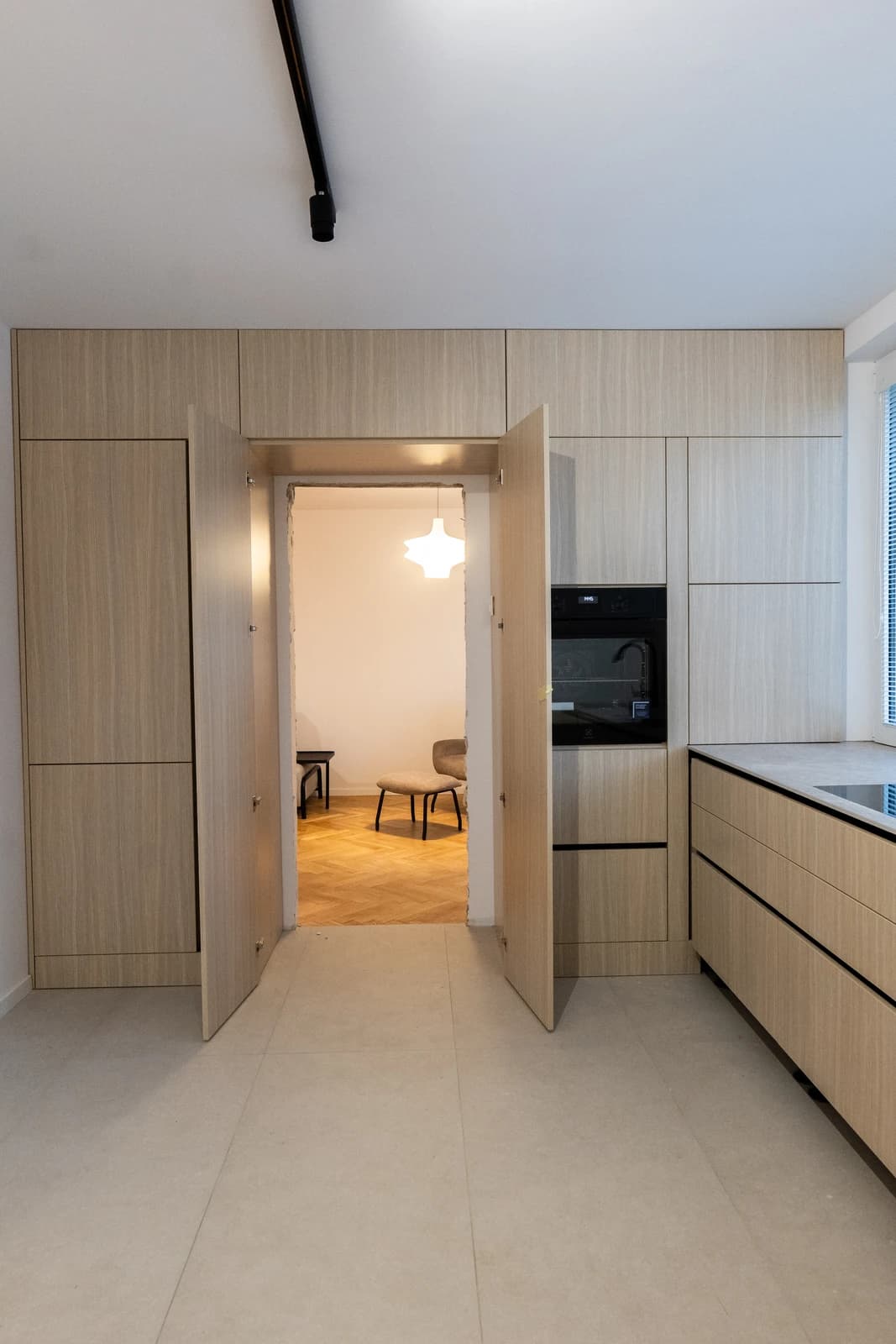 Štýlová tmavá kuchyňa s moderným osvetlením, zlatými akcentmi a elegantným jedálenským stolom.