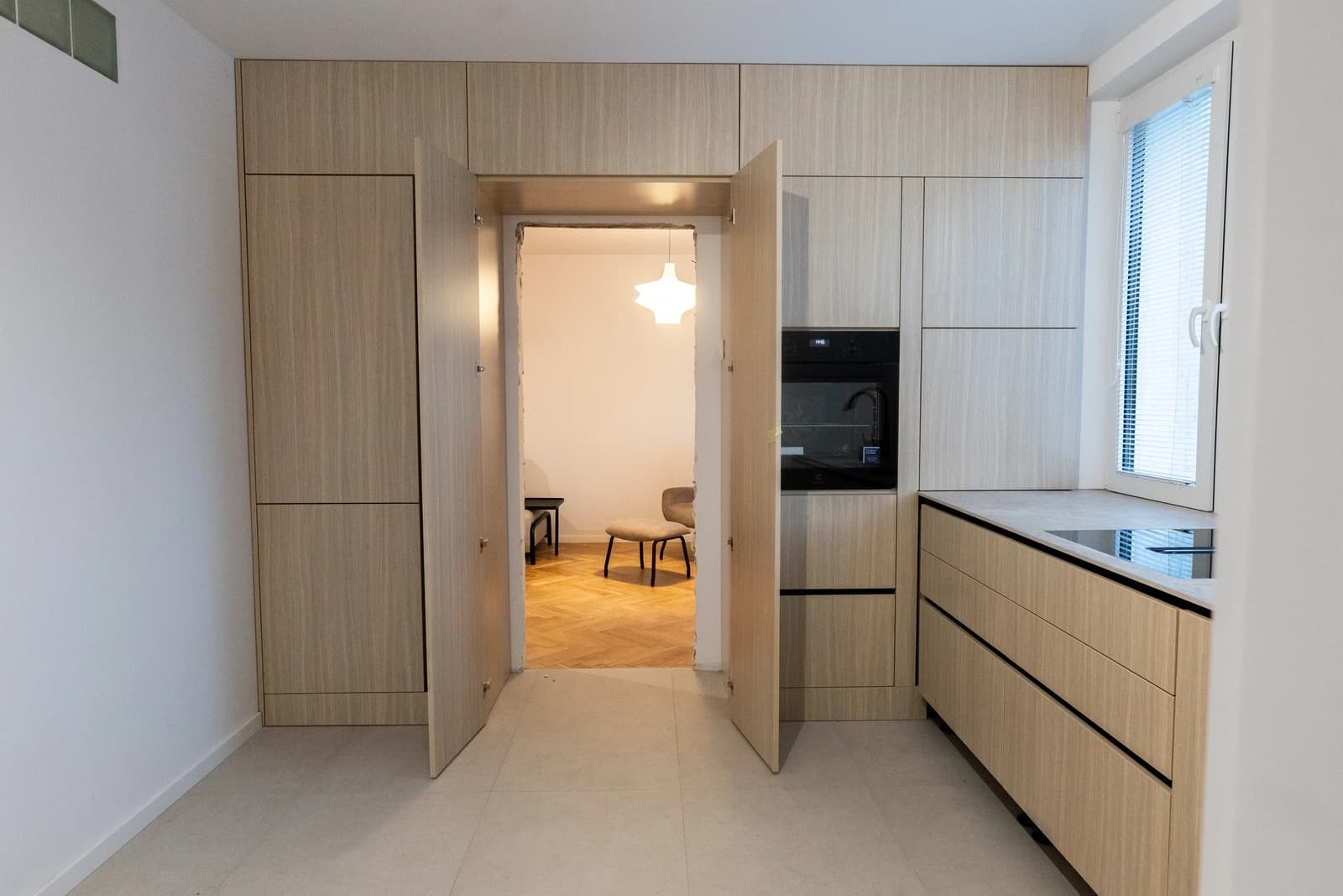 Štýlová tmavá kuchyňa s moderným osvetlením, zlatými akcentmi a elegantným jedálenským stolom.