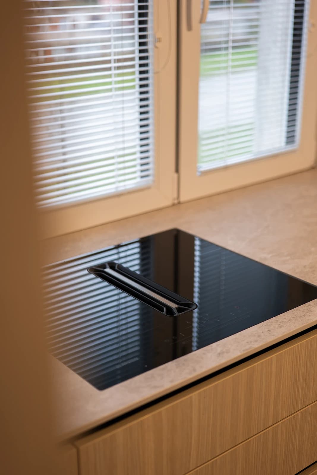 Štýlová tmavá kuchyňa s moderným osvetlením, zlatými akcentmi a elegantným jedálenským stolom.