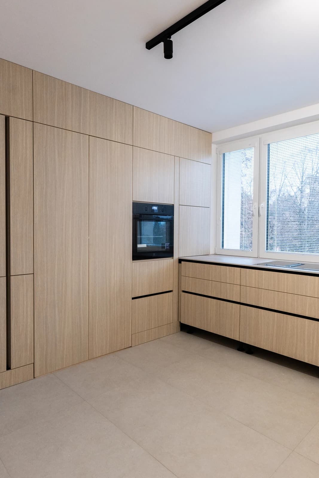 Štýlová tmavá kuchyňa s moderným osvetlením, zlatými akcentmi a elegantným jedálenským stolom.